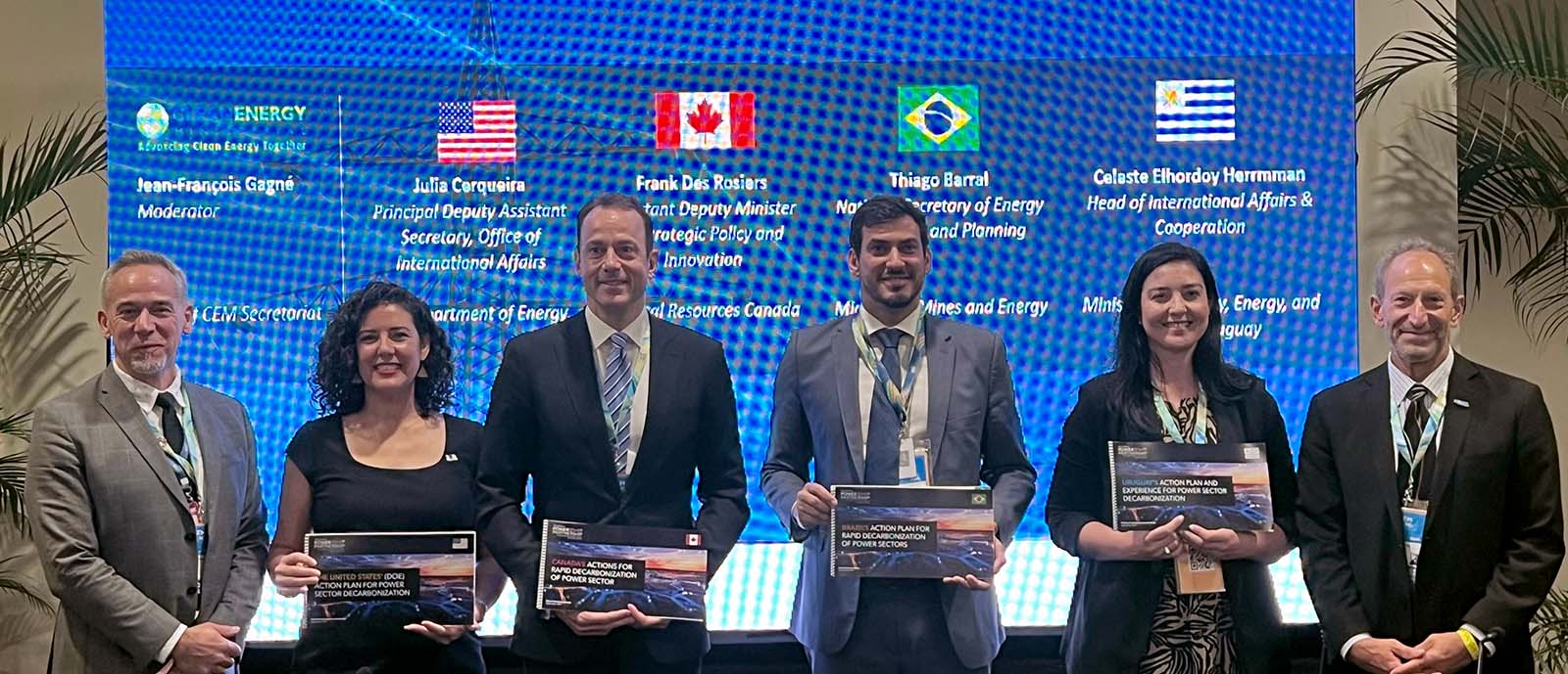 Six people pose for a group photo. Four of them hold copies of the climate action plans for different countries.